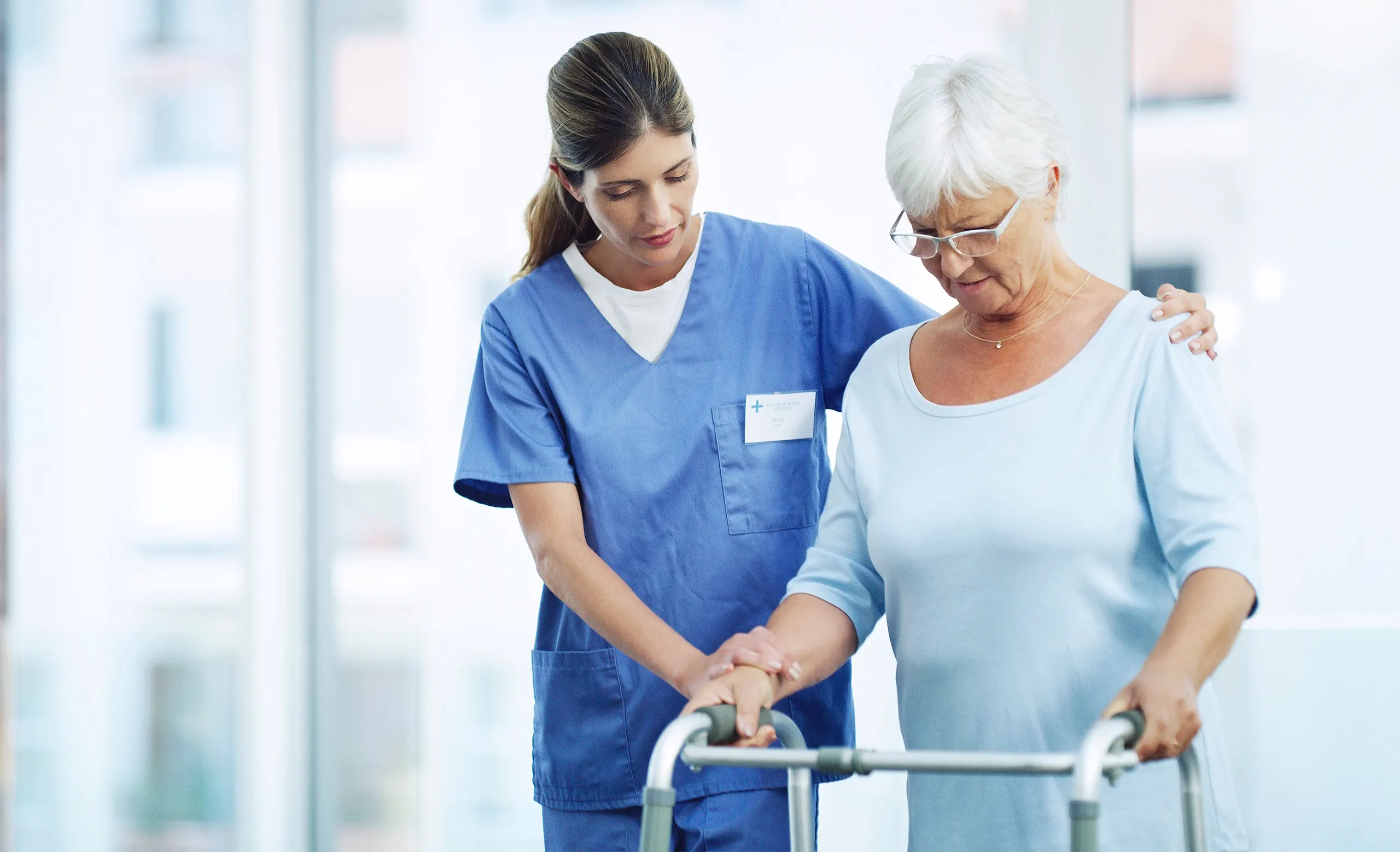 Member of nursing staff walking next to and guiding elderly woman using a walker