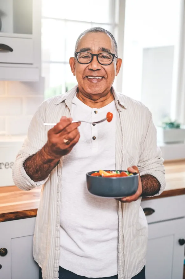 Man standing in kitchen smiling, holding a bowl ready to eat