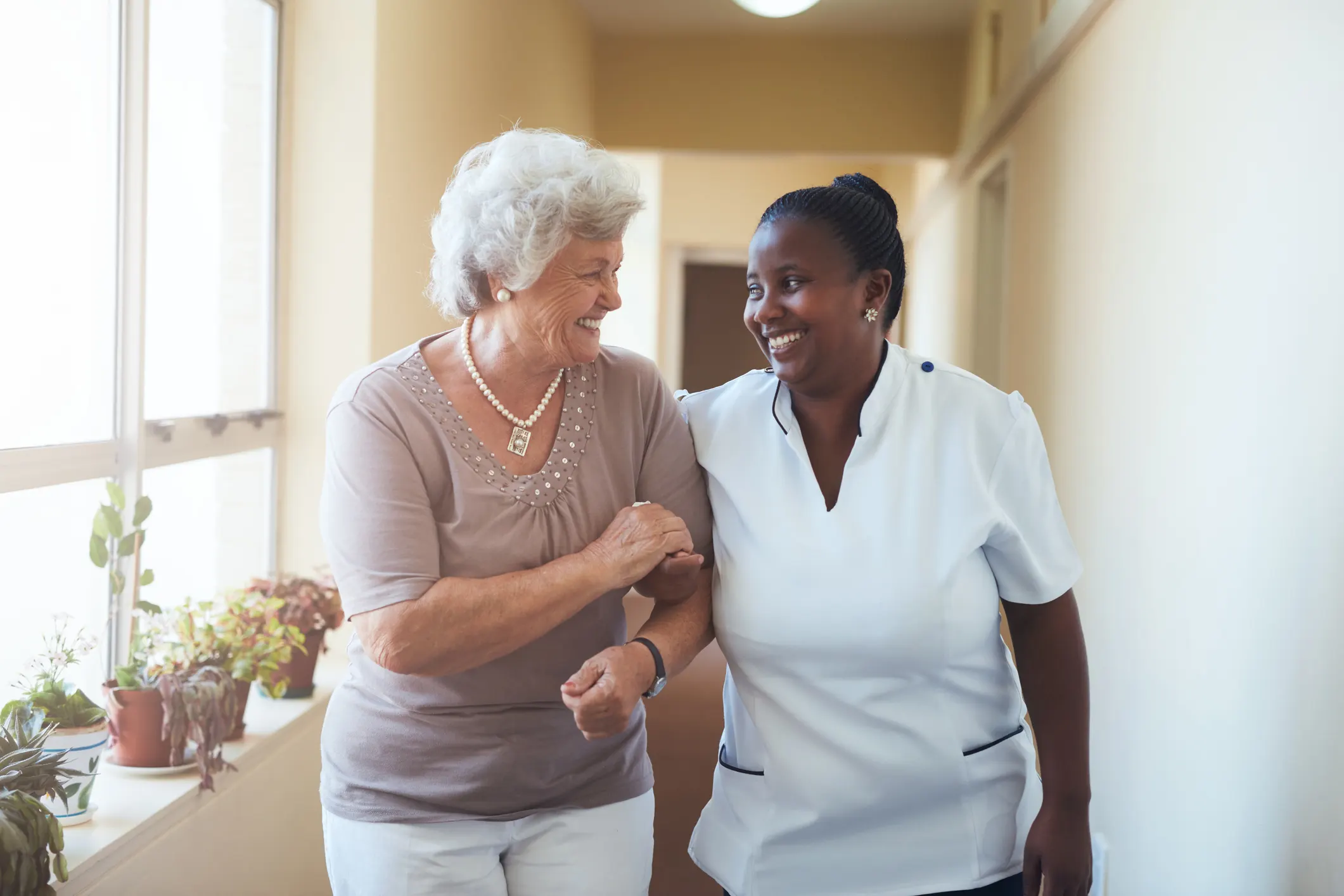 Assisted living resident walking with nurses aide down the hallway, arm in arm