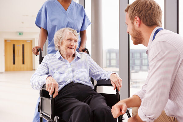 Male doctor down on one knee speaking to an elderly woman in a wheelchair