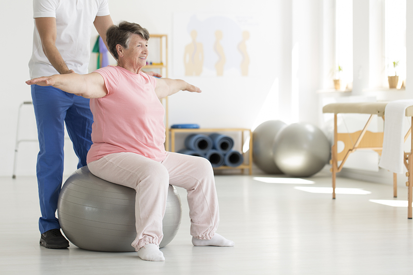Patient in Rehabilitation therapy sitting on a fit ball practicing balance