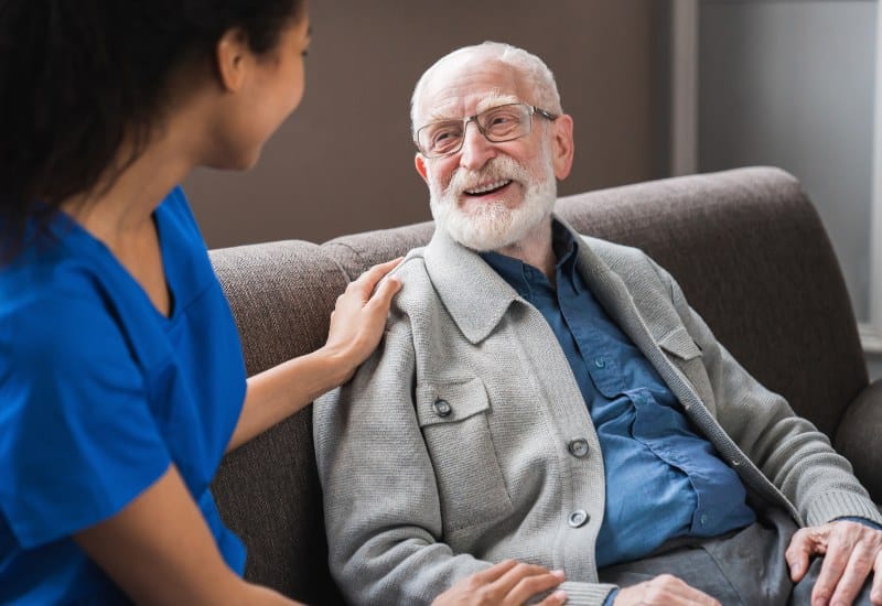 A caregiver and a smiling elderly man on a sofa featuring Palliative & Hospice Care in Mesquite, TX