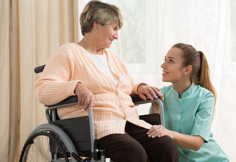 A caregiver smiling warmly with an elderly woman in a wheelchair, featuring respite care in Mesquite